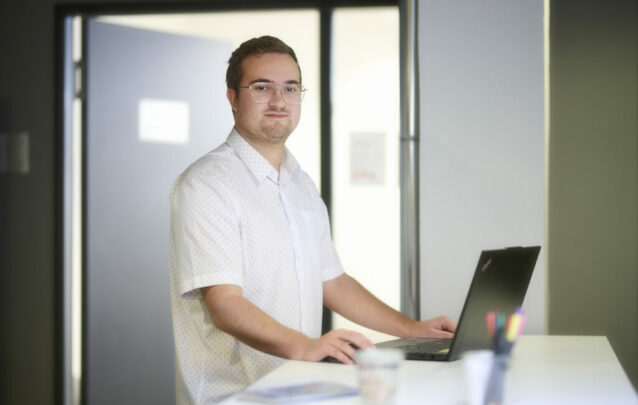 Joshua Seidler in weißem Hemd mit Brille, der am Laptop stehend arbeitet