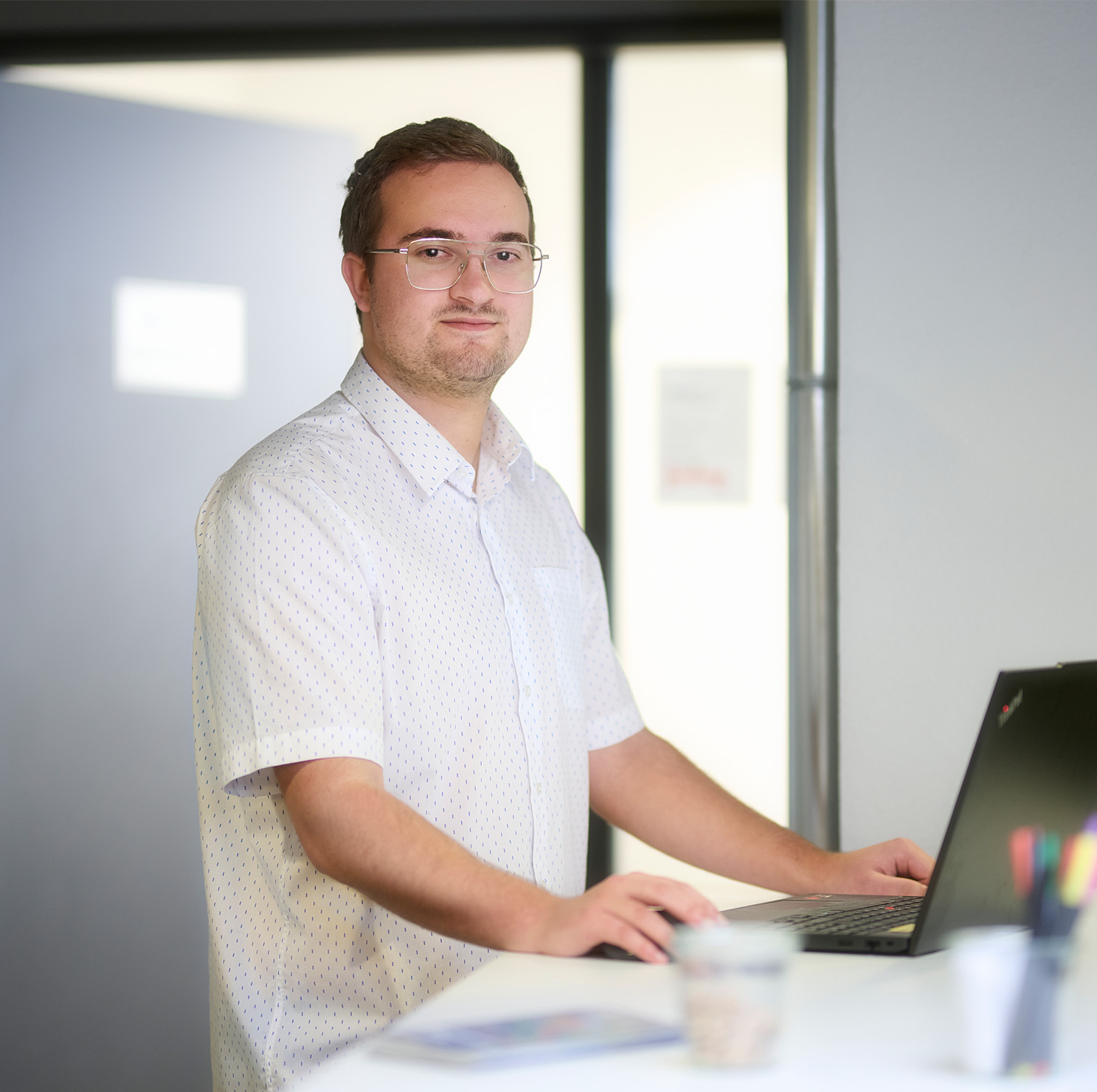 Joshua Seidler in weißem Hemd mit Brille, arbeitet am Laptop stehend